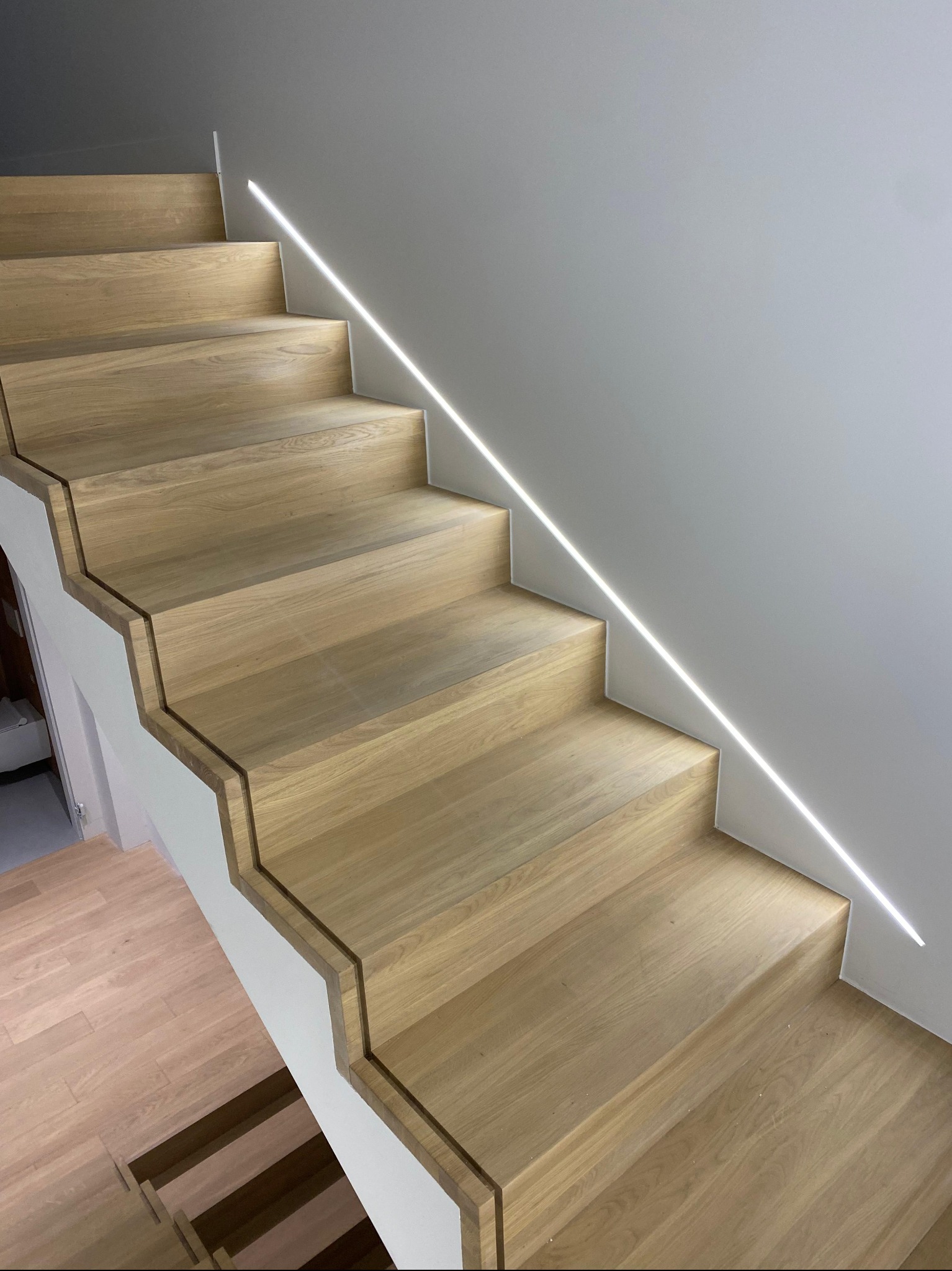 Nowoczesne schody z jasnego drewna z subtelnym oświetleniem LED wzdłuż ściany, minimalistyczny design, widok z dołu, jasne wnętrze.
