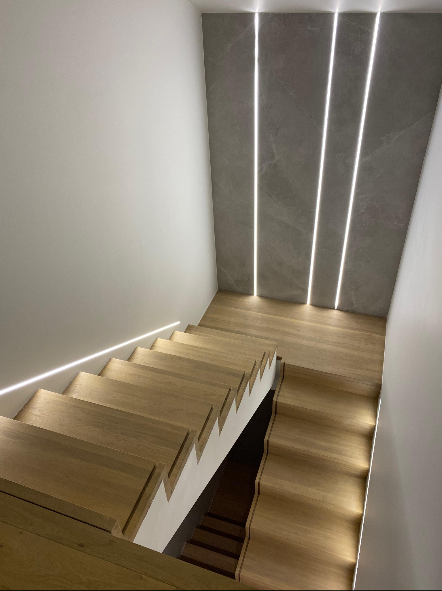 Nowoczesne schody z drewna z podświetleniem LED na ścianie z szarego kamienia. Minimalistyczny design, widok z góry.