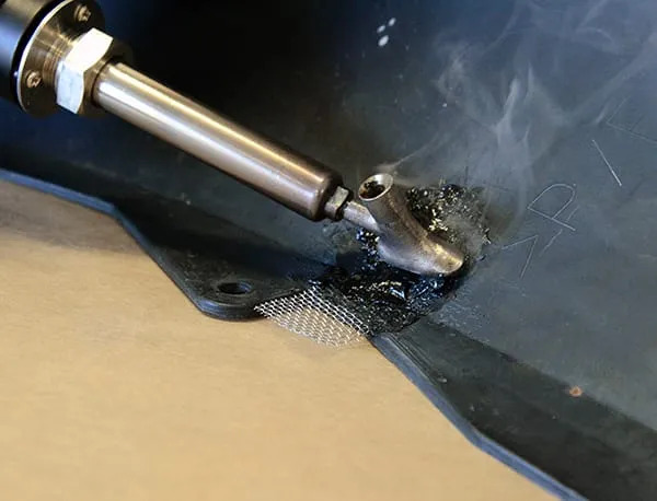 Naprawa plastiku z użyciem lutownicy i siatki wzmacniającej. Dym unosi się znad miejsca łączenia. Widoczne ślady po naprawie na czarnym elemencie.