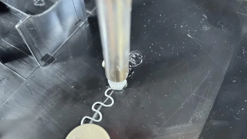 Proces łączenia elementów z tworzywa sztucznego za pomocą specjalistycznego urządzenia aplikującego spoiwo w zygzakowaty wzór na czarnej powierzchni.