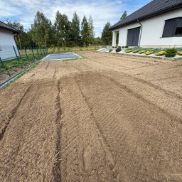 Iskra System Bartłomiej Kiedrzynek - Przygotowany teren pod trawnik w Częstochowie. W tle dom z ciemną dachówką, widoczne ślady opon po maszynach. Grządki wyrównane, gotowe do siewu trawy.