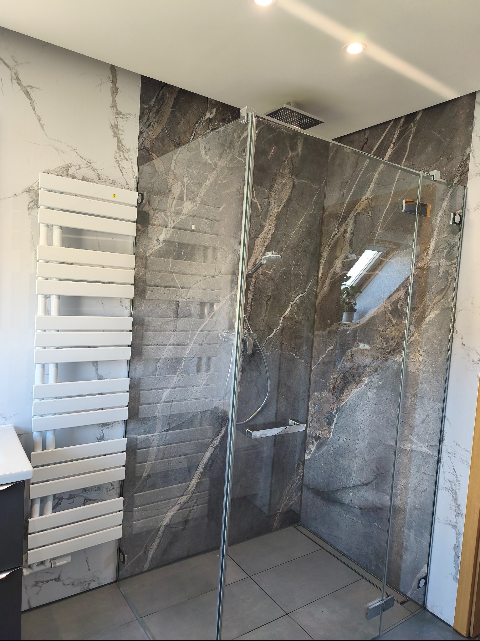 Nowoczesna kabina prysznicowa z marmurowymi płytkami i grzejnikiem drabinkowym w wykończonej łazience. Widoczne detale armatury i oświetlenia.