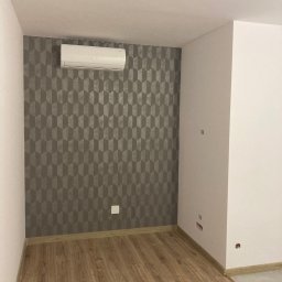 Atamanchuk Denys - Pokój po remoncie: parkiet, ściana z geometryczną tapetą, klimatyzator. Widoczne gniazdka elektryczne. Minimalistyczny design, jasne kolory, świeżo wykończone wnętrze.
