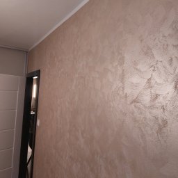 Atamanchuk Denys - Beżowa ściana z dekoracyjną strukturą, widoczna z perspektywy narożnika pokoju, z fragmentem drzwi po lewej stronie. Subtelne oświetlenie podkreśla fakturę.