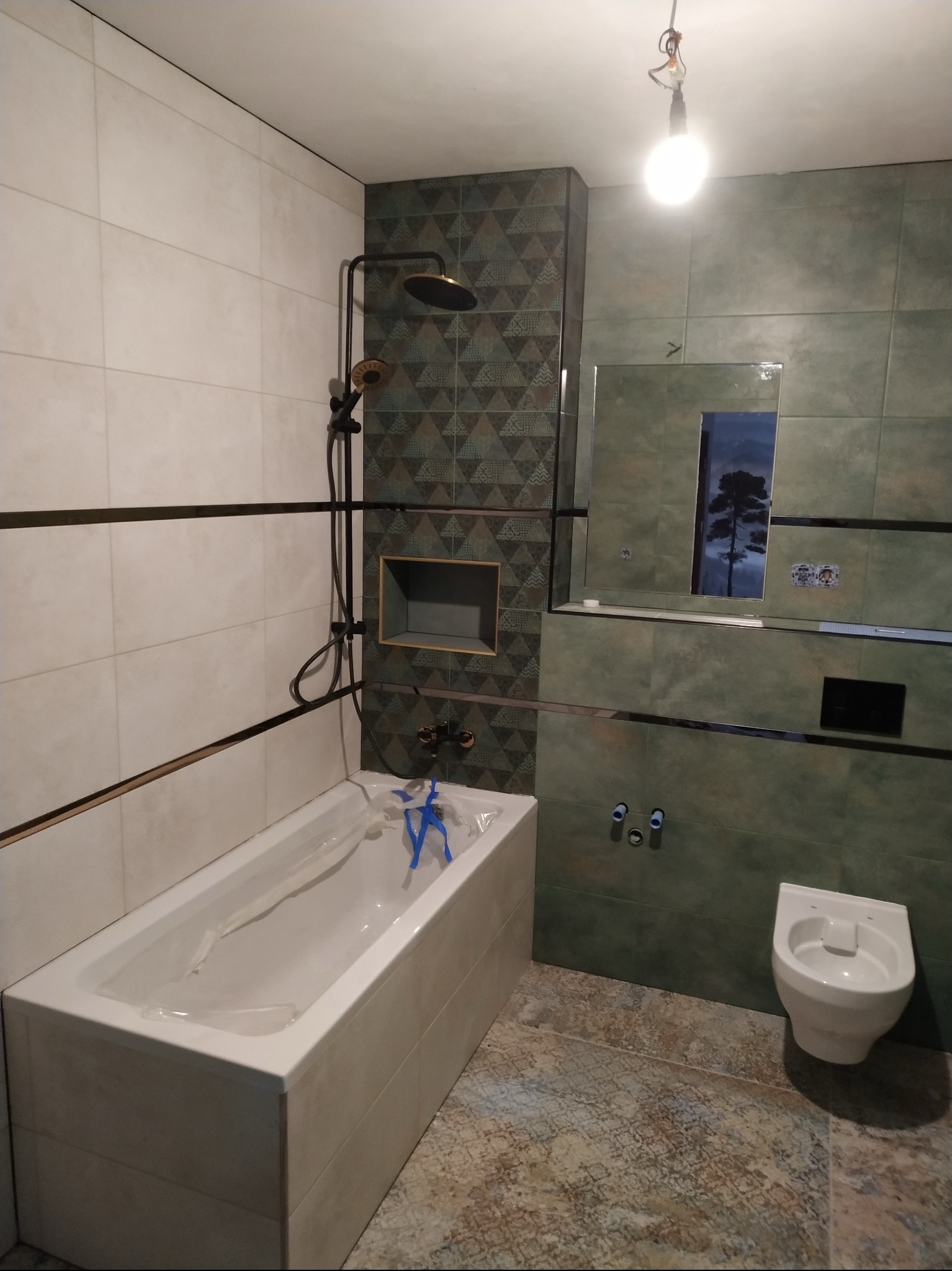 Nowoczesna łazienka z wanną, toaletą i prysznicem w odcieniach bieli i zieleni. Uwagę zwracają geometryczne wzory na płytkach i czarna armatura.