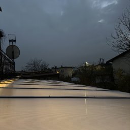 DomLabsStudio - Zadaszenie z poliwęglanu w pochmurny dzień, widok z góry na tle zabudowań i anteny satelitarnej. Delikatne światło odbija się od powierzchni.
