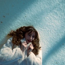 Pavlo LUXO - Kobieta w futrze leży na śniegu, ujęcie z góry. Ciemne włosy kontrastują z bielą otoczenia. Na śniegu widoczne drobne zanieczyszczenia i cień.