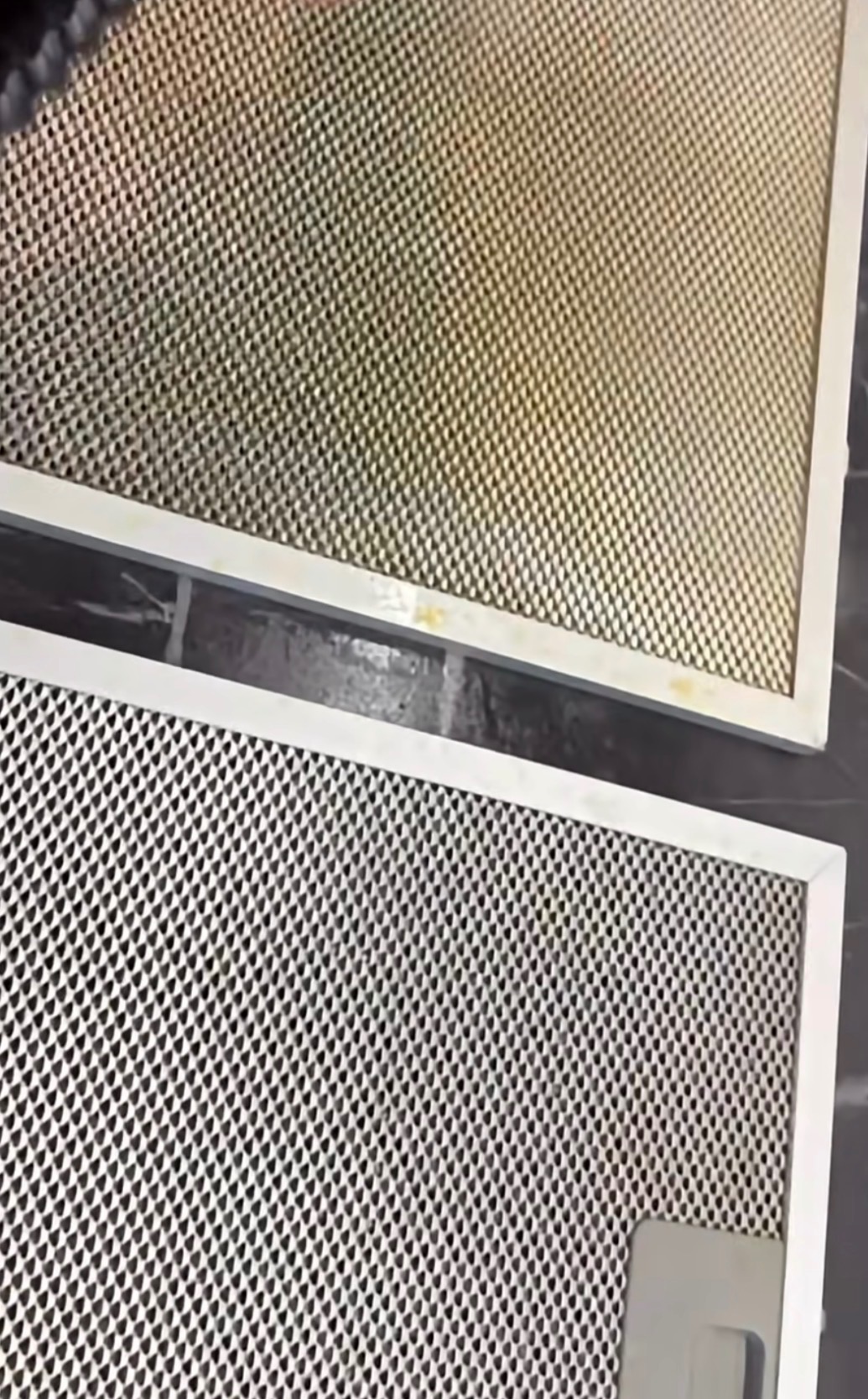 Dwa filtry okapu kuchennego: górny zabrudzony, z widocznymi plamami tłuszczu, dolny czysty, z regularną siatką. Ukazane na ciemnym tle.