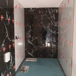 SIGMA SPÓŁKA Z OGRANICZONĄ ODPOWIEDZIALNOŚCIĄ - Łazienka w trakcie remontu: położone płytki imitujące marmur w odcieniach bieli i czerni, z użyciem klipsów poziomujących. Widoczna hydroizolacja podłogi.