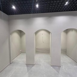 SIGMA SPÓŁKA Z OGRANICZONĄ ODPOWIEDZIALNOŚCIĄ - Wnętrze biura po remoncie: świeżo pomalowane ściany w odcieniach szarości, trzy symetryczne łukowe przejścia, czarny sufit kasetonowy z oświetleniem punktowym.