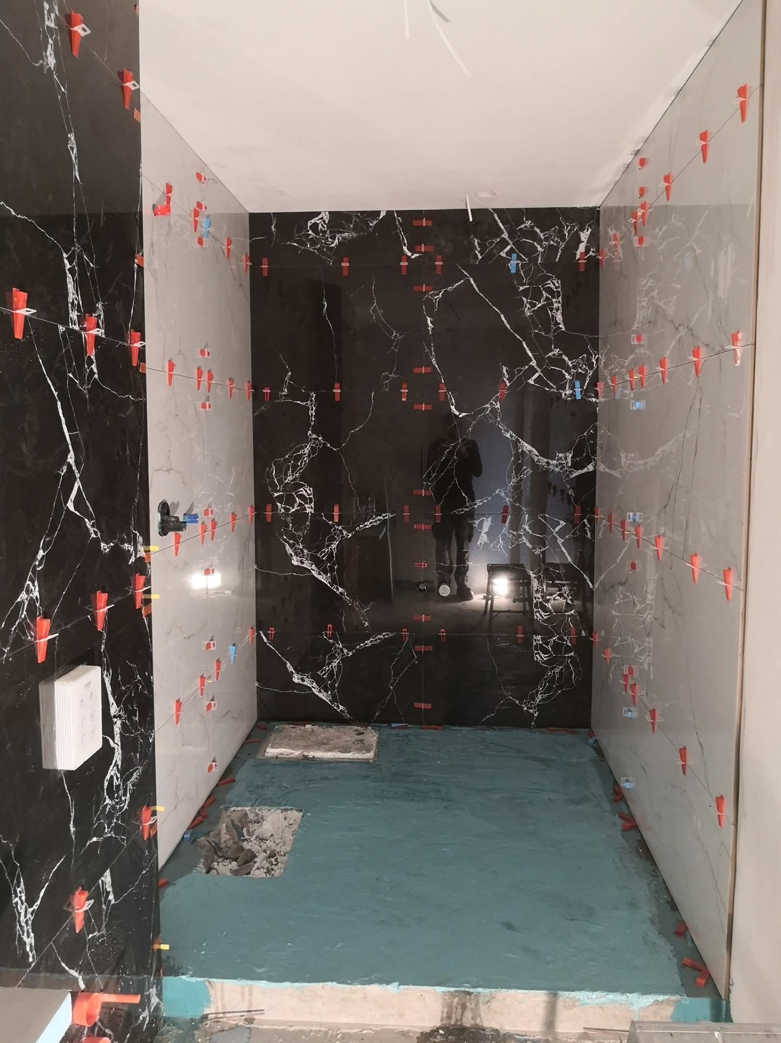 Łazienka w trakcie remontu: położone płytki imitujące marmur w odcieniach bieli i czerni, z użyciem klipsów poziomujących. Widoczna hydroizolacja podłogi.