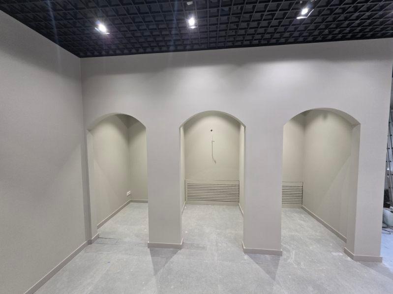 Wnętrze biura po remoncie: świeżo pomalowane ściany w odcieniach szarości, trzy symetryczne łukowe przejścia, czarny sufit kasetonowy z oświetleniem punktowym.