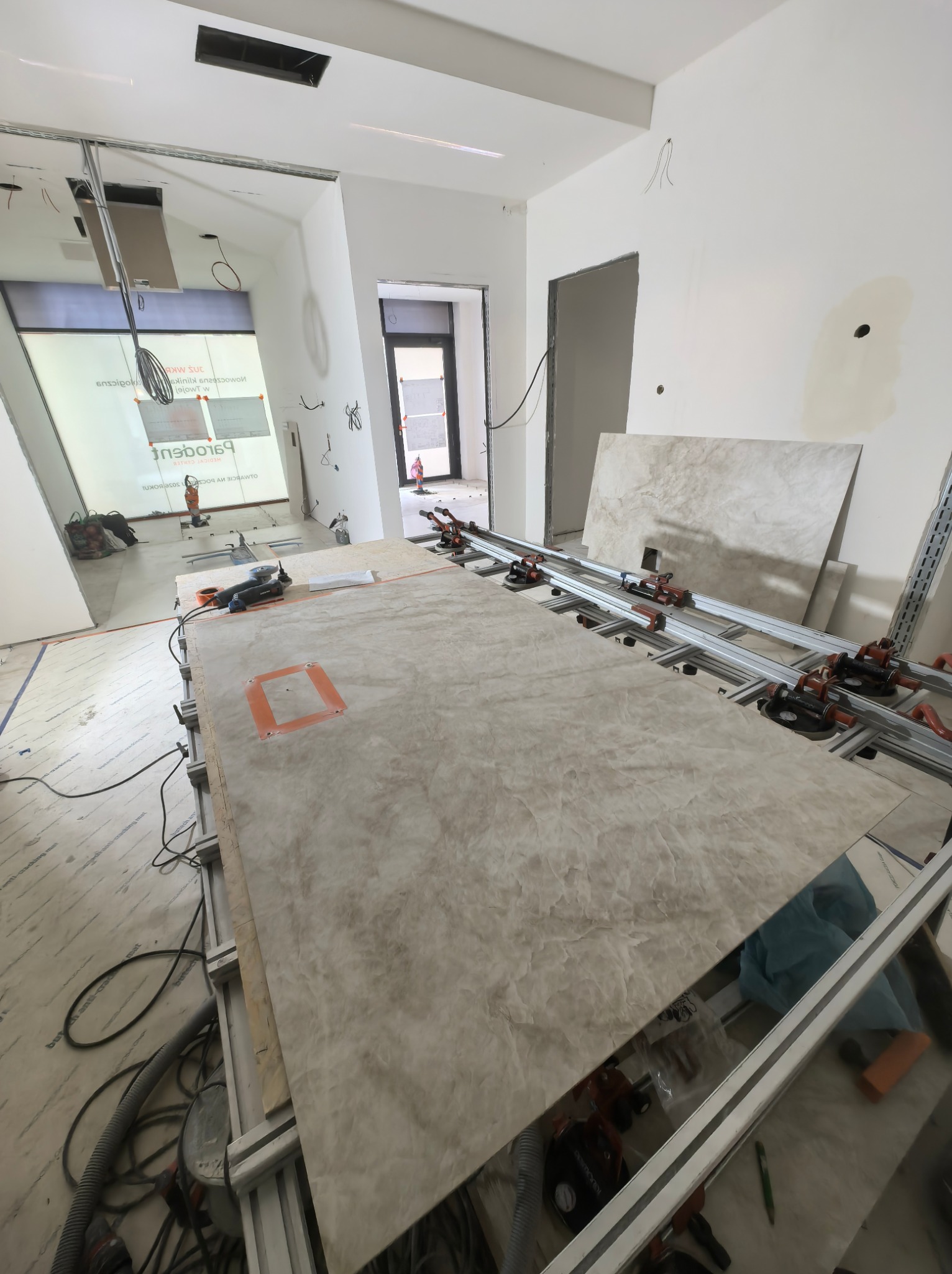 Płyta z efektem marmuru na stole roboczym z narzędziami w jasnym wnętrzu w trakcie wykańczania. Widoczne przewody i elementy instalacji.