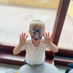 FANIMACJE Patrycja Jankowska - Uśmiechnięty chłopiec z pomalowaną twarzą w motywy zwierzęce, wyciąga ręce do przodu, stojąc przy oknie. Widoczne ślady farby na dłoniach i koszulce.