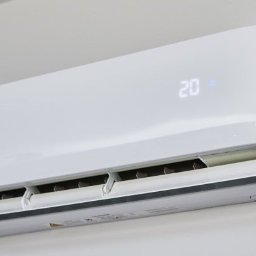 COOLBIX Tomasz Kulbicki - Biała klimatyzacja ścienna z wyświetlaczem temperatury 20 stopni Celsjusza, zamontowana na jasnej ścianie. Widoczne żaluzje wylotu powietrza.