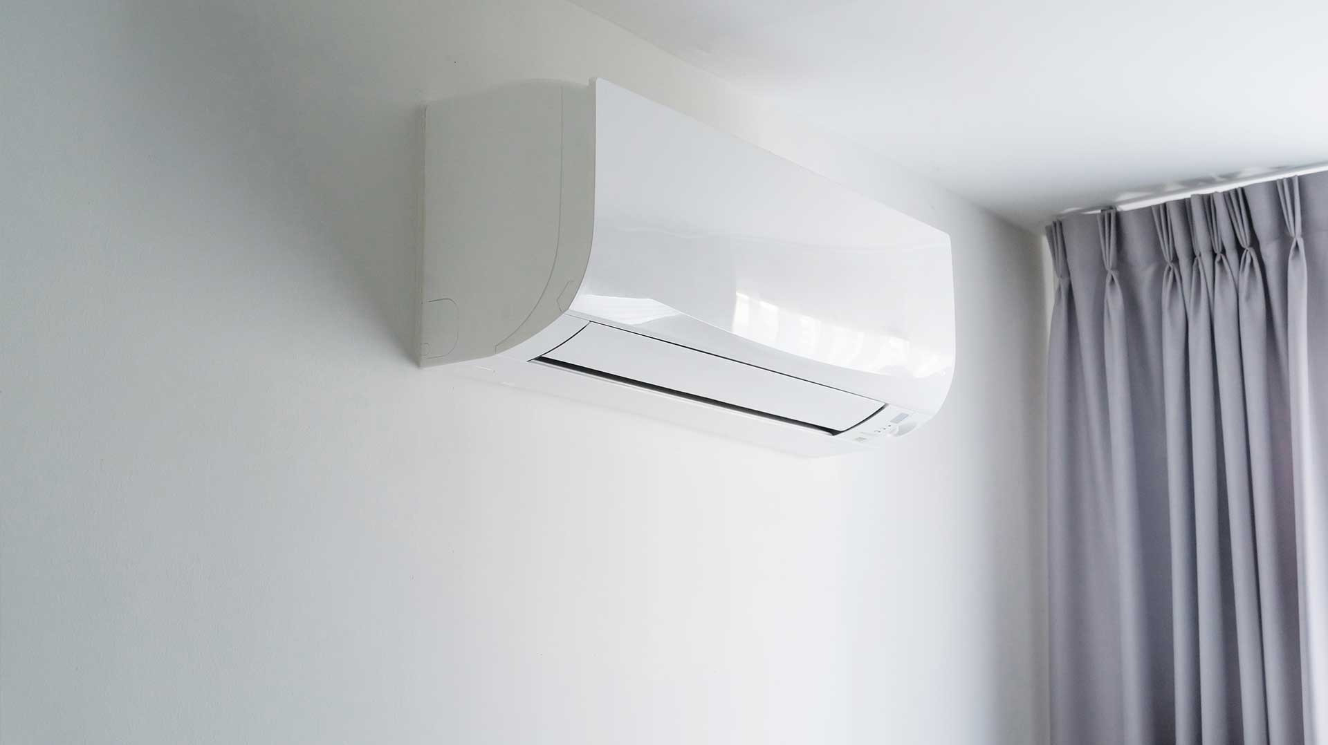 Nowoczesny, biały klimatyzator ścienny zamontowany w jasnym pomieszczeniu z szarymi zasłonami. Minimalistyczny design, czyste linie, subtelne oświetlenie.