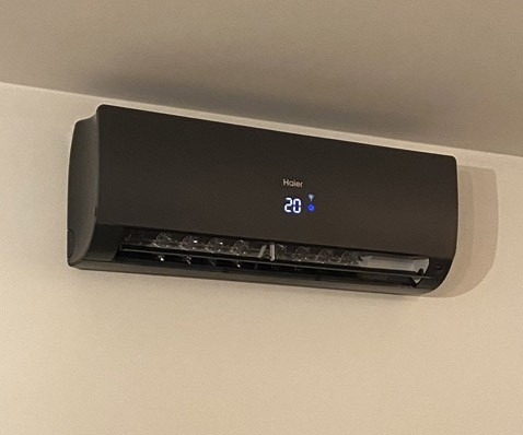 Czarny klimatyzator Haier na ścianie, wyświetlający temperaturę 20 stopni. Nowoczesny design, minimalistyczne wnętrze, widok z dołu.