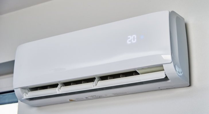 Biała klimatyzacja ścienna z wyświetlaczem temperatury 20 stopni Celsjusza, zamontowana na jasnej ścianie. Widoczne żaluzje wylotu powietrza.