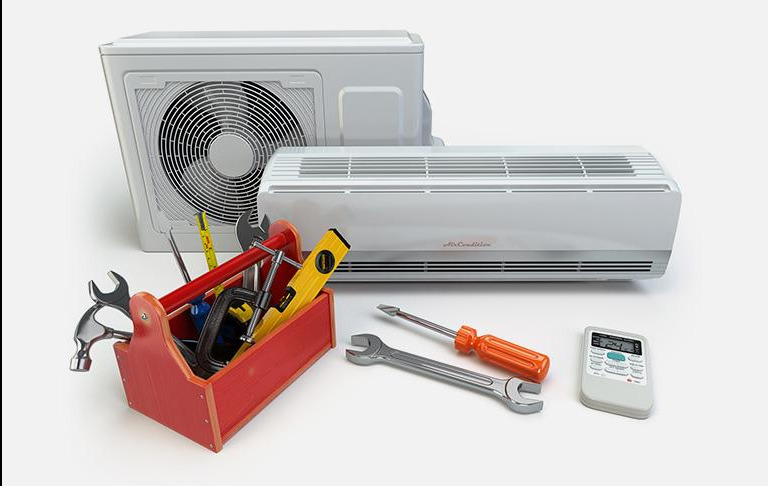 Klimatyzator split z czerwonym kuferkiem narzędzi, kluczami i poziomnicą na białym tle. Widoczny pilot do sterowania klimatyzacją.