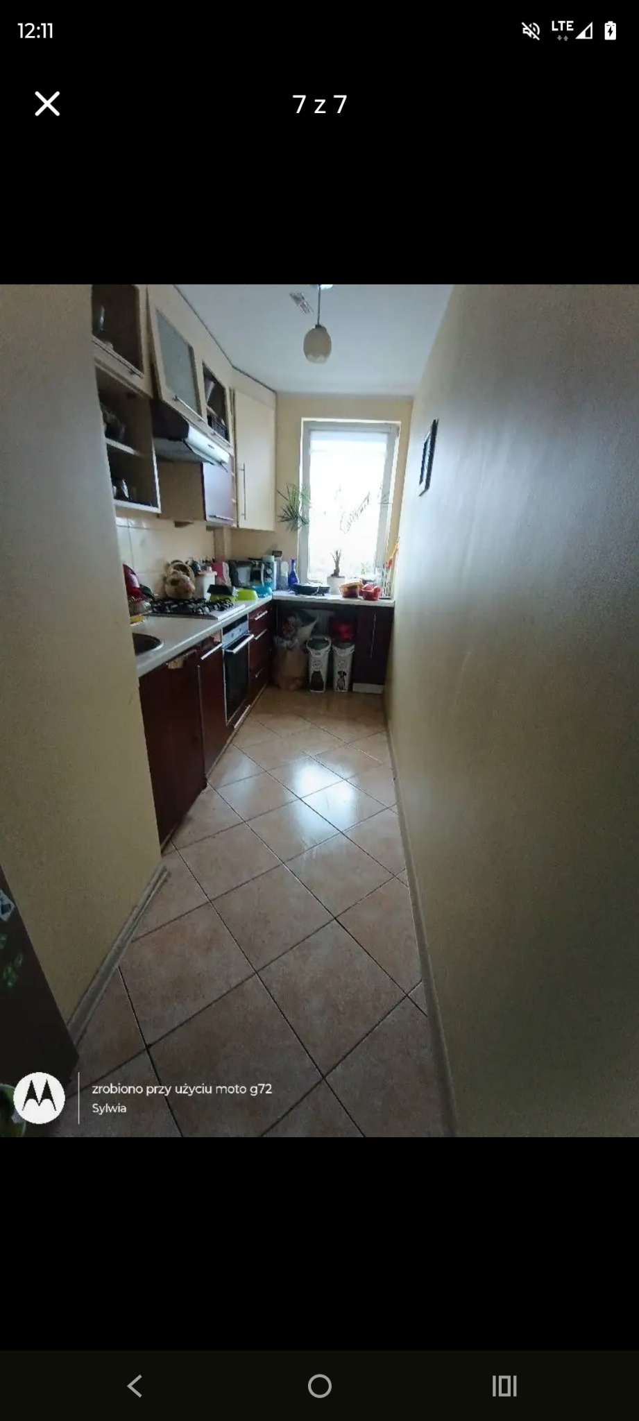 Ustawna kuchnia w bloku po sprzątaniu: brązowe szafki, beżowe ściany, okno z rośliną. Widok na czystą podłogę z płytek i uporządkowany blat.