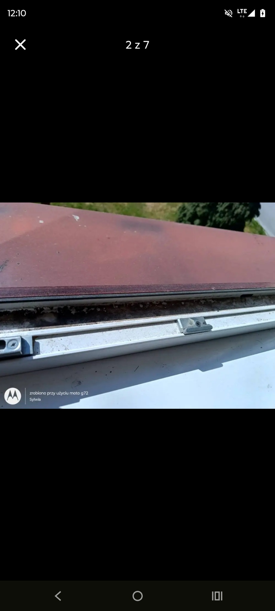 Brudne okno PCV z widocznymi zabrudzeniami na ramie i uszczelce, zieleń w tle. Perspektywa z góry, ukazująca detale wymagające czyszczenia.