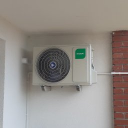 SniMer Piotr Gajos - Zamontowany klimatyzator Kaisai na białej ścianie balkonu, z widocznymi rurami instalacyjnymi i stolikiem z farbami. Widok z dołu, jasne oświetlenie.