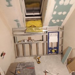 S-Bud - Poddasze w trakcie adaptacji: okno dachowe, metalowy stelaż pod zabudowę, częściowo zagruntowane ściany, narzędzia pracy na podłodze. Widok z dołu.