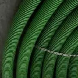 ZI System - Zielone, karbowane rury wentylacyjne przymocowane do surowego, betonowego sufitu za pomocą białej opaski zaciskowej. Widok z dołu, instalacja w trakcie montażu.