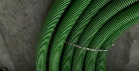 Zielone, karbowane rury wentylacyjne przymocowane do surowego, betonowego sufitu za pomocą białej opaski zaciskowej. Widok z dołu, instalacja w trakcie montażu.