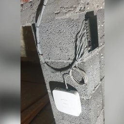 WINKAM - Montaż Monitoringu, Alarmy, Wideodomofony, Smart Home, Instalacja Kamer - Bartosz Gruszka Rybnik - Zamontowany router i switch z okablowaniem na szarej ścianie z betonu komórkowego w Rybniku. Instalacja sieciowa w trakcie realizacji.