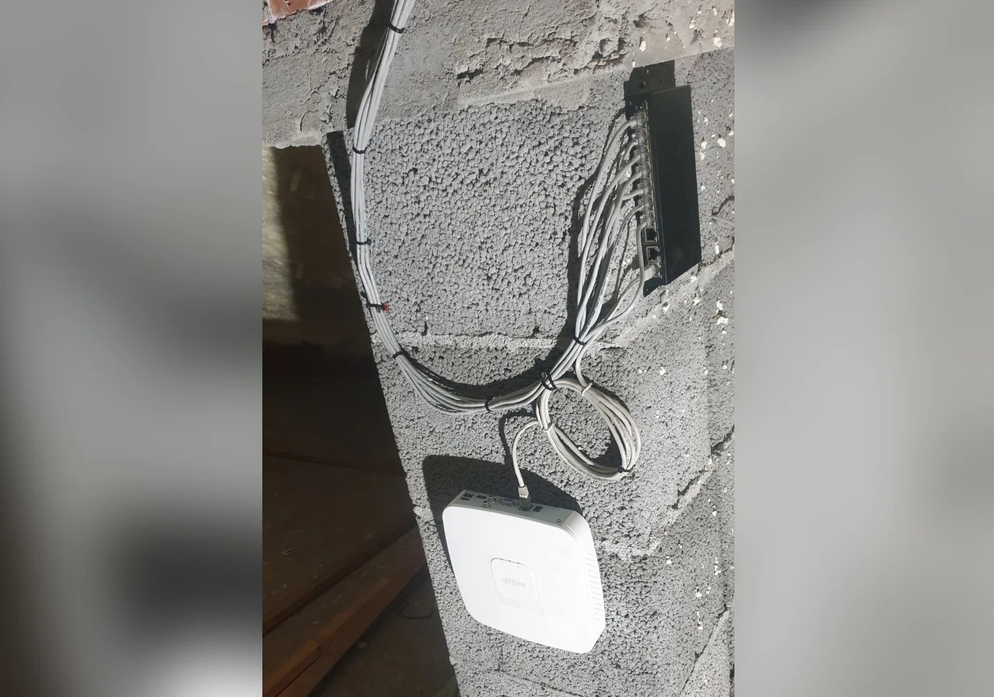 Zamontowany router i switch z okablowaniem na szarej ścianie z betonu komórkowego w Rybniku. Instalacja sieciowa w trakcie realizacji.