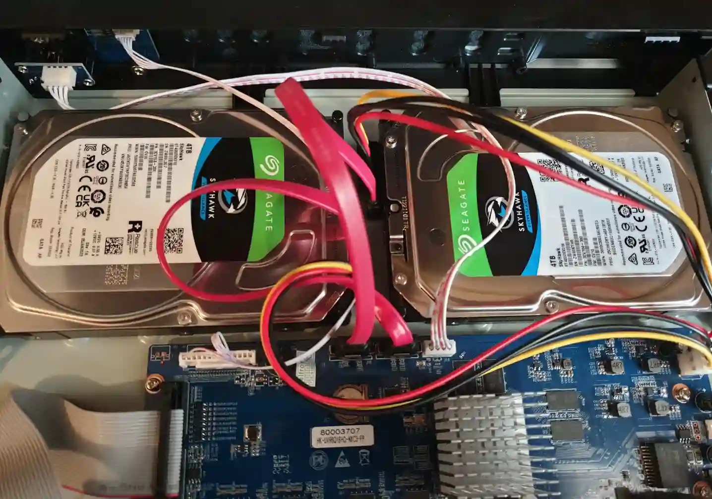 Wnętrze rejestratora monitoringu z dwoma dyskami twardymi Seagate Skyhawk 4TB, podłączonymi kablami SATA. Widoczna płyta główna urządzenia.