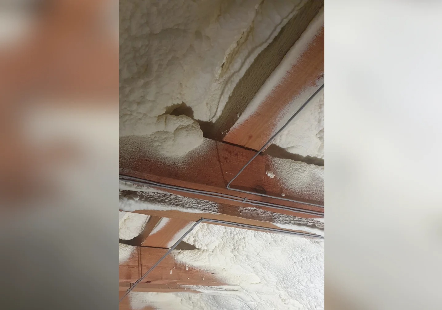 Poddasze ocieplone pianą PUR, widoczne drewniane belki i szare przewody. Izolacja natryskowa pokrywa konstrukcję dachu, tworząc jednolitą warstwę.