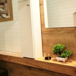 PMP Paweł Paciora - Nowoczesna łazienka z białą szafką, drewnianym blatem, ceglaną ścianą i dekoracjami: szklanka z napojem i miniaturowe drzewko bonsai w białej doniczce.