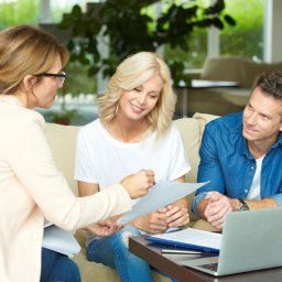 Paweł Sokulski Zalew Możliwości - Spotkanie agentki nieruchomości z parą klientów omawiających dokumenty przy laptopie w jasnym wnętrzu. Uśmiechnięta kobieta w centrum, naturalne światło.
