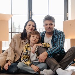 Paweł Sokulski Zalew Możliwości - Uśmiechnięta rodzina siedzi na podłodze w nowym domu, otoczona kartonami. Duże okno w tle. Radosny nastrój po przeprowadzce.