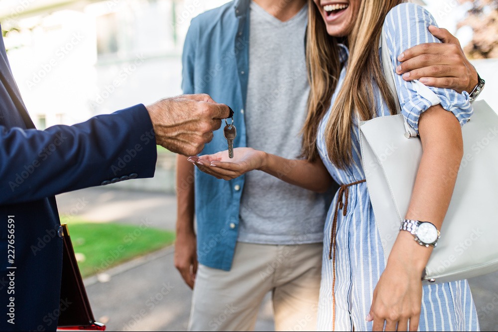 Przekazanie kluczy do mieszkania uśmiechniętej parze przez agenta nieruchomości. Widoczny fragment umowy. Symboliczny moment wręczenia kluczy do nowego domu.
