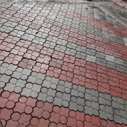 Doktor Bruk - Czerwono-szara kostka brukowa ułożona we wzór, widoczna z perspektywy. Częściowo mokra powierzchnia sugeruje niedawne czyszczenie.