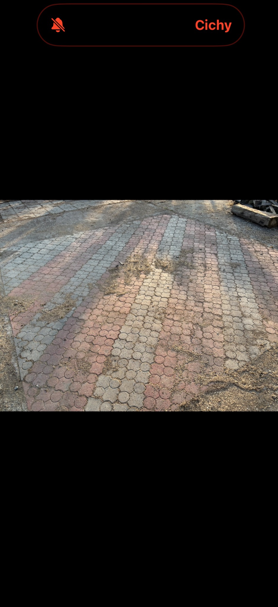 Ułożona kostka brukowa w odcieniach szarości i czerwieni, pokryta piaskiem i drobnymi zabrudzeniami. Widoczne nierówności i ślady użytkowania.