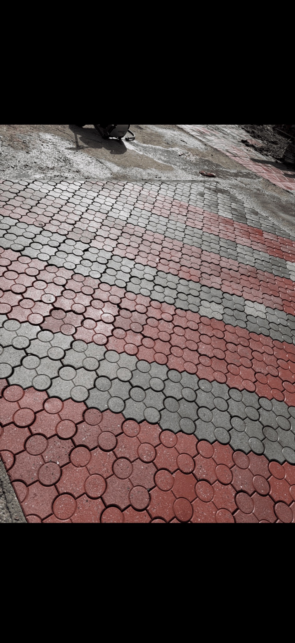 Czerwono-szara kostka brukowa ułożona we wzór, widoczna z perspektywy. Częściowo mokra powierzchnia sugeruje niedawne czyszczenie.