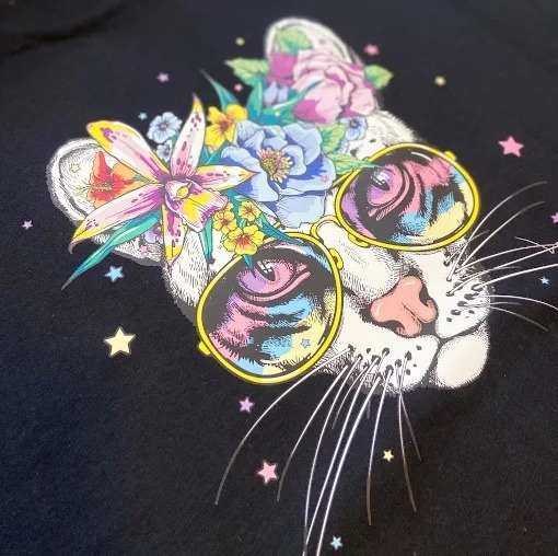 Czarna koszulka z nadrukiem kota w okularach i kwiatach, stylizowane na retro, z drobnymi gwiazdkami w tle. Unikalny wzór.