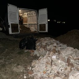 Czyściuś-Trans - Nocne wywożenie gruzu busem: otwarte drzwi, wnętrze wypełnione odpadami, obok sterta gruzu i czarne worki. Słabe oświetlenie, widoczne elementy budynku w tle.