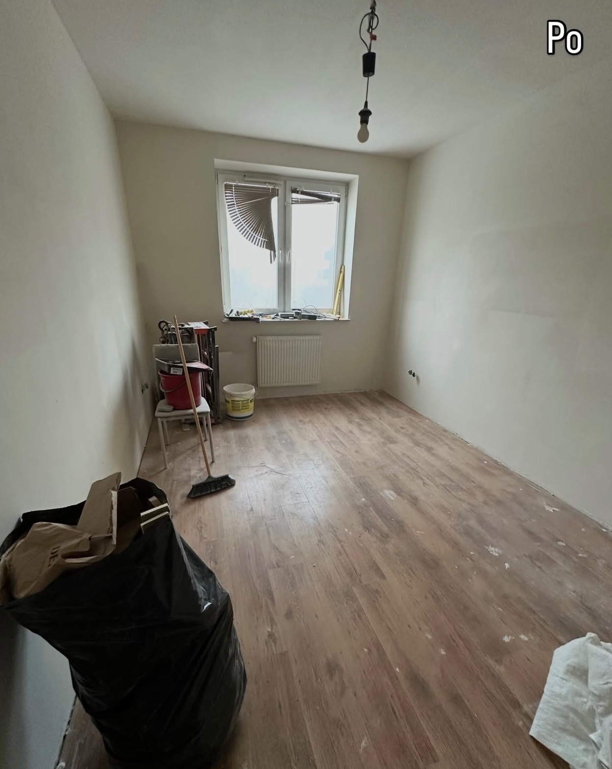 Pokój po remoncie: świeżo pomalowane ściany, nowa podłoga z paneli, widoczne narzędzia i akcesoria malarskie. Ujęcie z perspektywy podłogi, z napisem 'Po' w rogu.