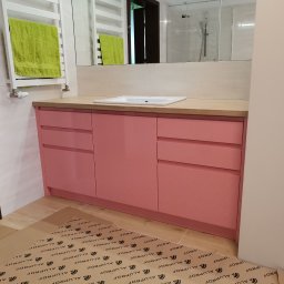 KERAD-MEBLE Dariusz Biliński - Różowa szafka łazienkowa z drewnianym blatem i białą umywalką w Olsztynie. Nad nią lustro, a obok grzejnik z zielonym ręcznikiem. Na podłodze folia ochronna.