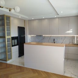 KERAD-MEBLE Dariusz Biliński - Jasna kuchnia z wyspą i złotymi akcentami: przeszklona witryna, marmurowy backsplash, drewniany blat. Nowoczesny design z oświetleniem LED.