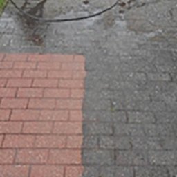 Holm Łukasz Mańka - Częściowo wyczyszczona, czerwona kostka brukowa, z widoczną różnicą między czystą a brudną powierzchnią. W tle wąż i fragment buta osoby czyszczącej.