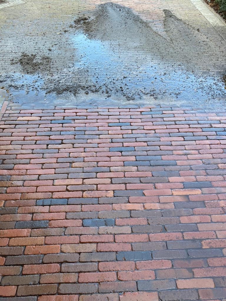 Częściowo umyta kostka brukowa z czerwonej cegły, widoczny brud i woda. Górna część powierzchni jeszcze nieumyta, dolna czysta. Perspektywa z dołu do góry.