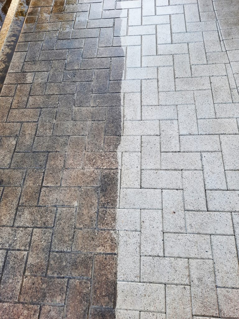 Kostka brukowa po czyszczeniu: połowa brudna, połowa czysta. Widoczny kontrast przed i po myciu, z bliska, wzór jodełki, mokra powierzchnia.