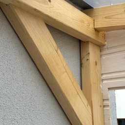Leszek Dulinski - Fragment drewnianej konstrukcji z belek, prawdopodobnie elementu tarasu lub pergoli, z widocznymi detalami łączeń i fakturą drewna na tle ściany.