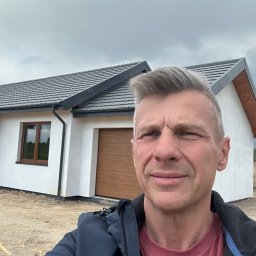 Leszek Dulinski - Nowoczesny, parterowy dom z garażem i drewnianymi elementami wykończeniowymi, uchwycony z bliska z perspektywy osoby stojącej przed budynkiem, pochmurne niebo w tle.